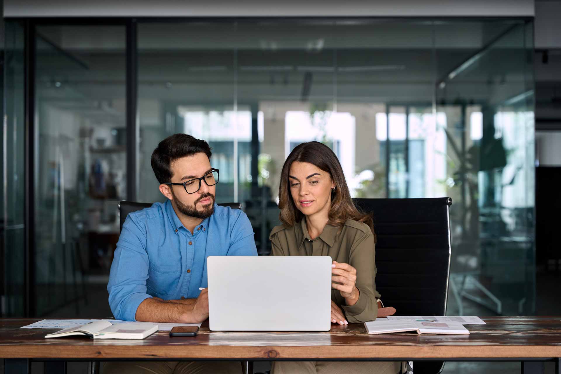 Zwei Personen arbeiten gemeinsam an einem Laptop in einem modernen Büro.