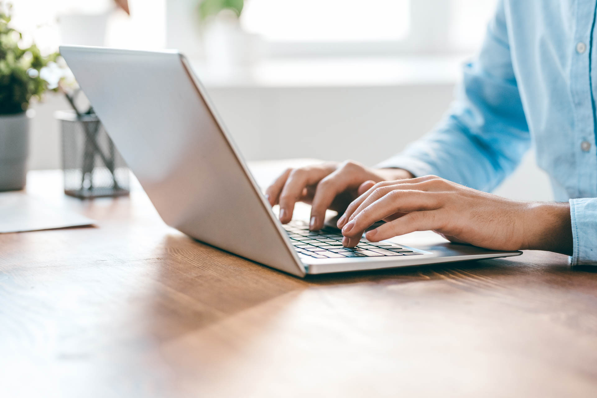 Hände eines jungen, modernen Büroleiters über der Tastatur eines Laptops während der Arbeit