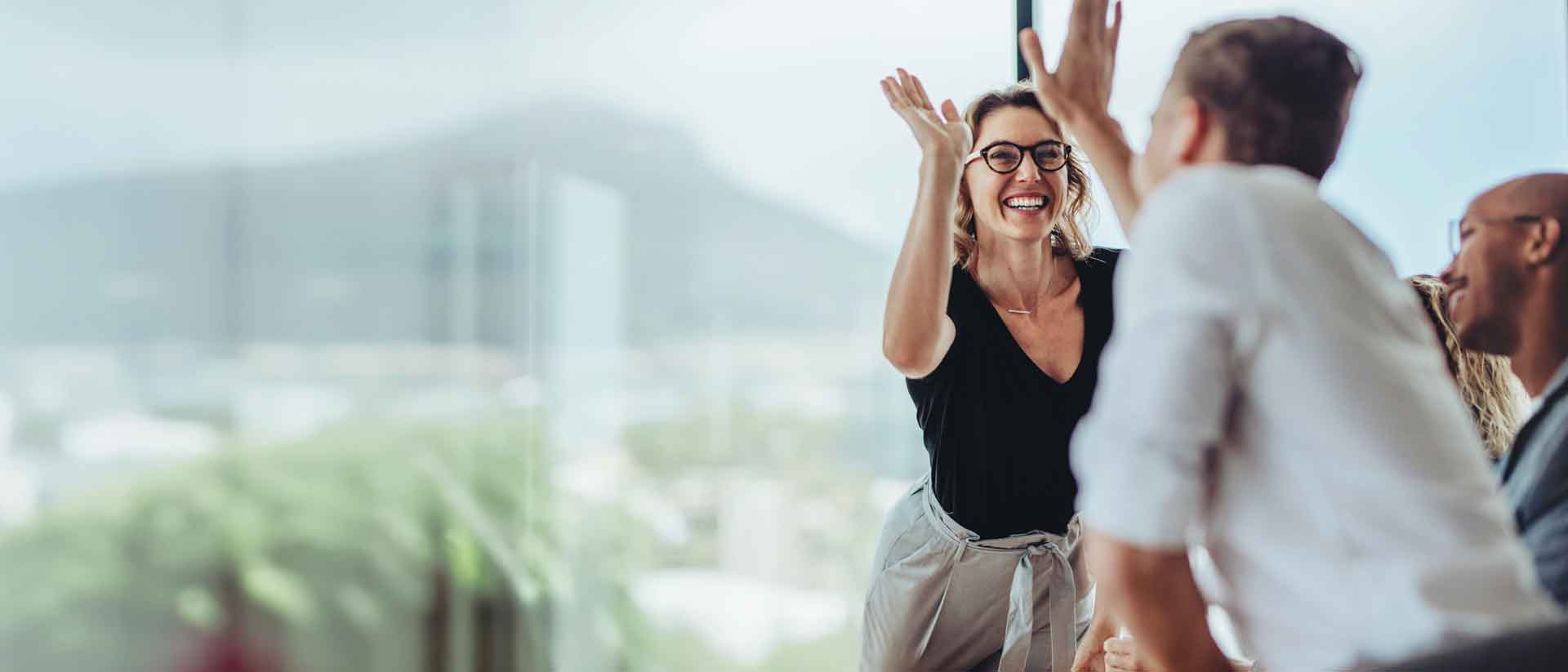 Eine fröhliche Frau gibt Kollegen High-Five, umgeben von Kollegen in einem hellen Büro.